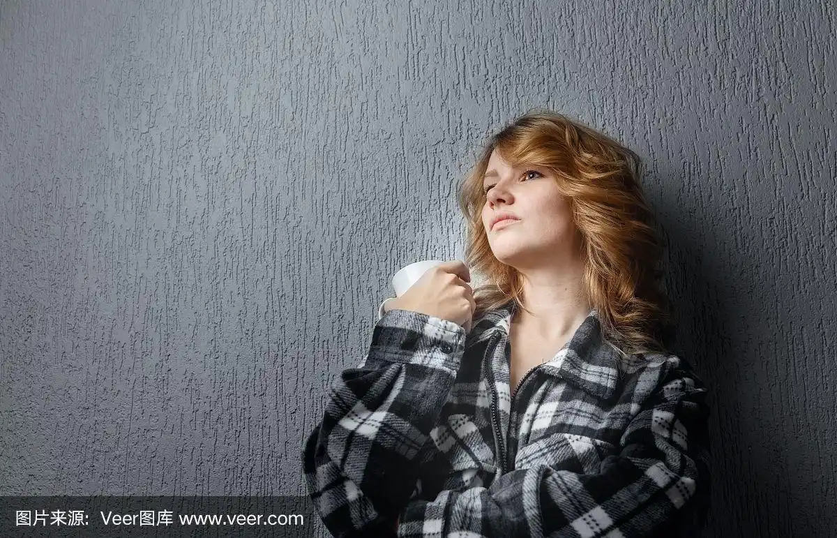 悲伤的年轻女子靠在灰色的墙上.