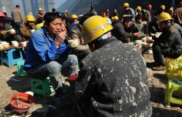光着膀子的农民工蹲着地上吃饭,啃馒头,城市的华丽