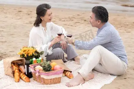 幸福的老年夫妇坐在海滩上野餐饮酒
