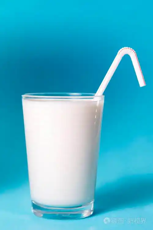 在蓝色背景查出的稻草的全杯牛奶
