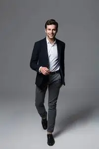 行走西装一个年轻的快乐商人,穿着一套西装,在灰色背景下摆着姿势