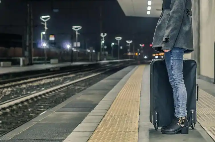 阳光下坐在车站一遍候车一边使用笔记本电脑的女孩