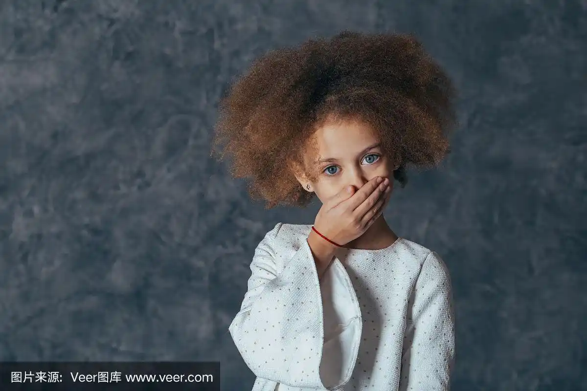 快乐的卷发女孩的大头照,微笑着看着相机.灰色的背景.