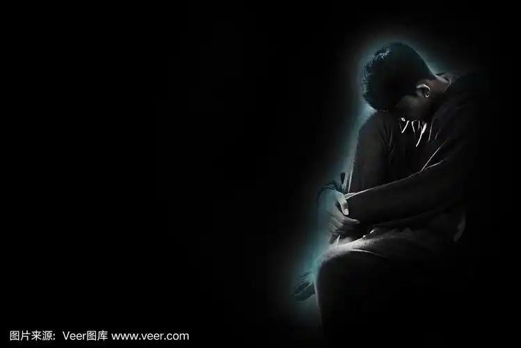 黑暗中,男孩低着头,胳膊绕着膝盖坐在房间的角落里