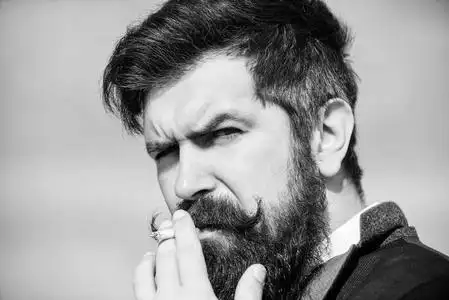 吸烟的影响留胡子的男人拿着香烟.留着胡子的潮人吸烟的天空背景.