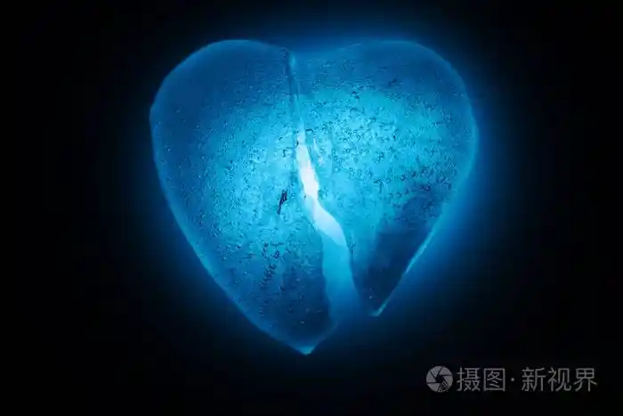 冰冻碎在半心象征蓝色特写在黑暗中在蓝色冷光中发光有气泡的冰的质地