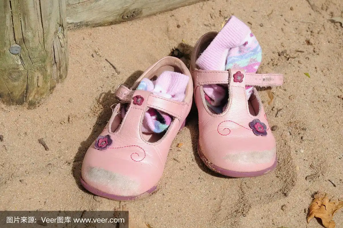 小女孩的粉色皮凉鞋和袜子在沙坑里