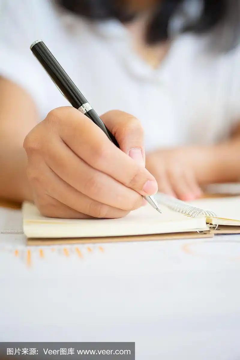 近距离拍摄的女商人的手拿着一支笔写在纸上的东西在办公室的前景.