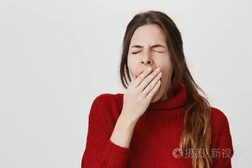 年轻可爱疲惫的女孩的肖像, 打哈欠与她的眼睛闭上, 遮住她的嘴, 隔着