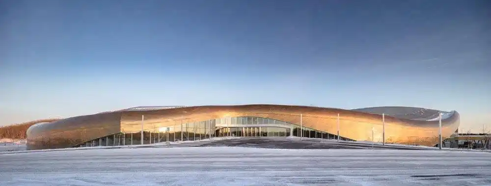 这座起伏的蛇形建筑拥有巨大的占地面积,有着闪闪发亮的黄铜带状外墙