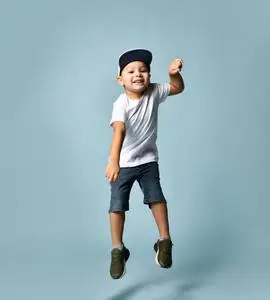 一个深色的小孩穿着白色t恤,牛仔短裤和卡其色运动鞋.