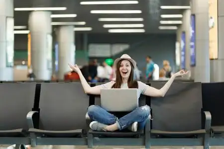 带着笔记本电脑,双腿交叉坐着,沉思着,摊开双手,等待在机场大厅