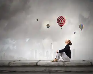 屋顶上的女商人坐在与五颜六色的气球飞行上面的大厦顶部的年轻俏丽的