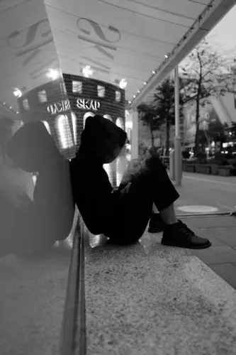 一个穿着时尚的青年坐在街头一边玩手机,一边抽烟,一边哆嗦