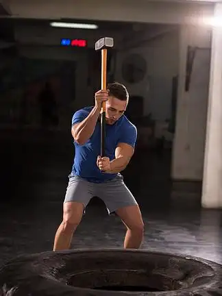 大锤轮胎在健身房用锤子和拖拉机轮胎击中年轻的肌肉男锻炼