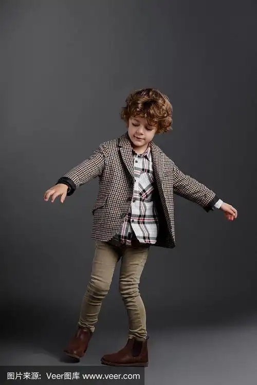 一个可爱的卷毛小男孩穿着古典服装在演播室跳舞,孤立在灰色的背景.