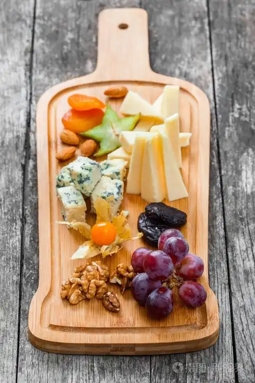 奶酪拼盘饰以梨蜂蜜核桃葡萄杨桃酸浆在砧板上木制的背景上小吃和酒
