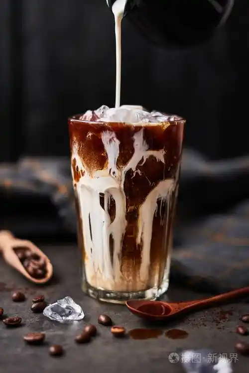 冰咖啡放在一个高杯子里,上面倒着奶油,咖啡豆放在黑色的木制背景下的