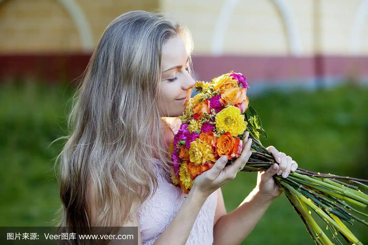 年轻漂亮的女人捧着一束鲜艳的花,姑娘闻着花香