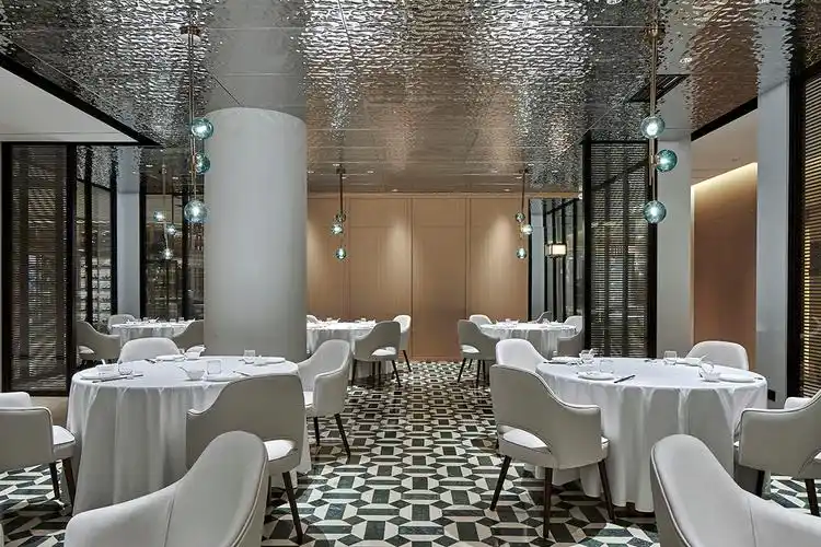 大厅用餐区域位于整个空间正中,银色光泽的金属顶面与白绿拼花的石材