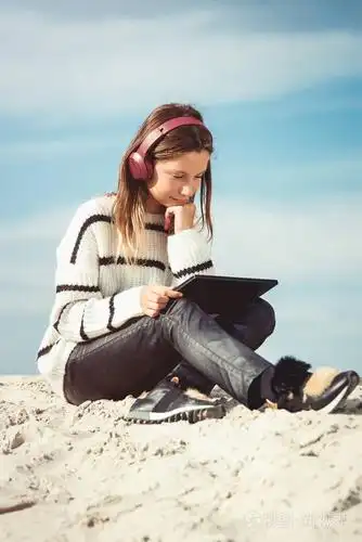 1 1岁的女孩戴着无线耳机, 在海滩上听着智能手机上的音乐.对着蓝天.