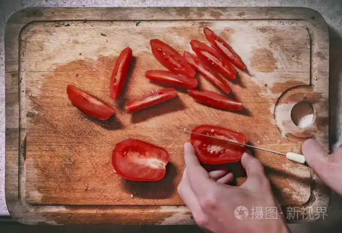 人手拿刀切切片红西红柿在又旧又脏的厨房切割板上准备沙拉顶景特写