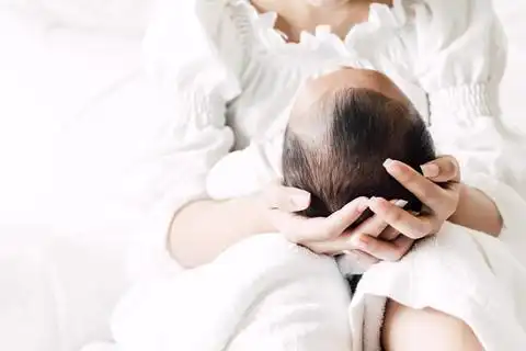 母亲抱着婴儿在她的怀里, 在一个白色的卧室.对家庭概念的爱