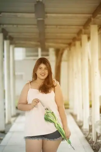 亚洲漂亮的笑脸脸胖女人姿势站立, 并持有雨伞在人行道上