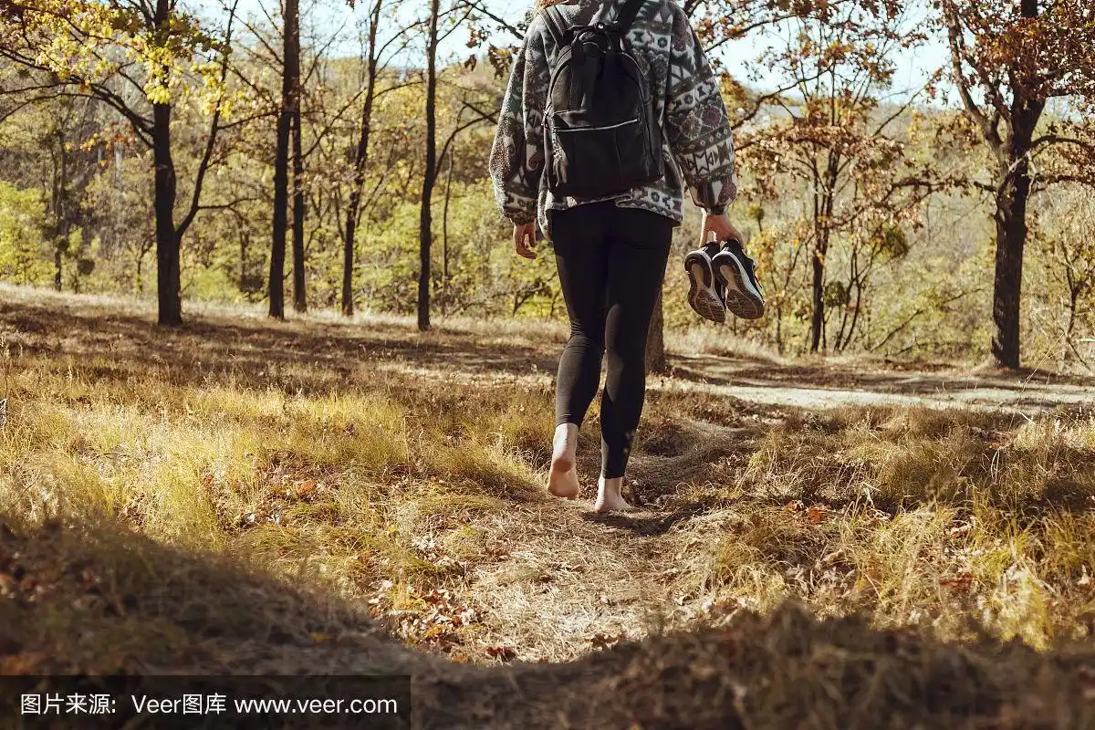美丽的年轻女孩赤脚穿着运动鞋走进森林.选择性对焦照片