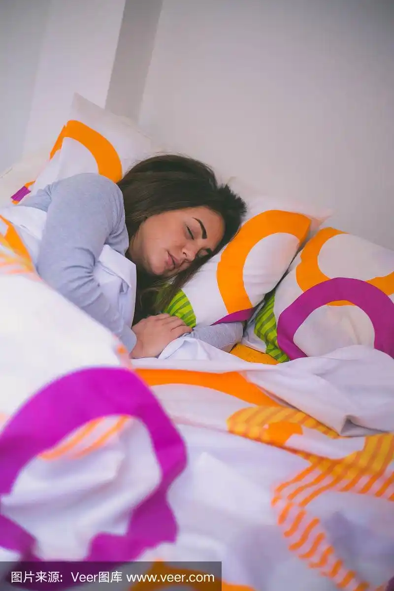 年轻的褐发女人盖着被子睡在床上