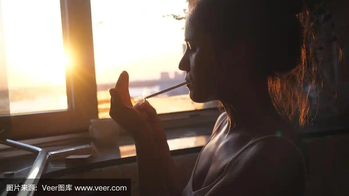 悲伤孤独的女人坐在窗前,在日落时分吸烟