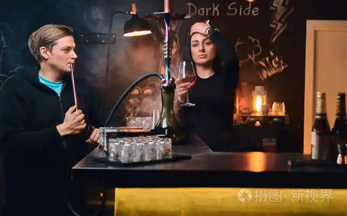 年轻夫妇在夜总会或酒吧放松穿着连帽衫的帅哥抽烟诱人的黑发女人喝酒