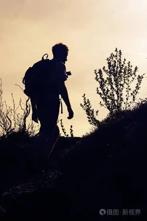 一个背包客的剪影在橙色傍晚的天空远足