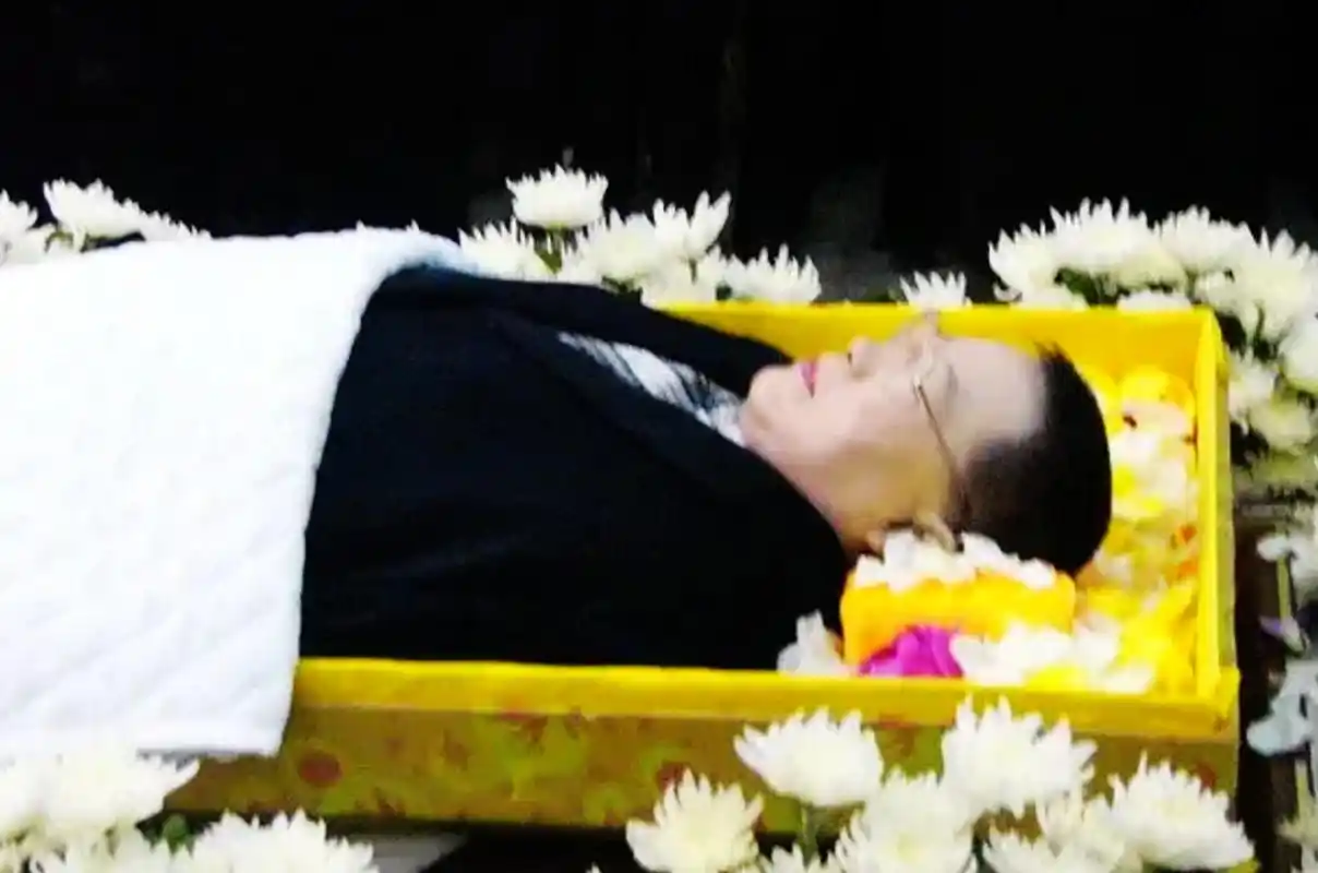 照片中,他戴着眼镜,身着黑色西装,安详地躺在花丛中.