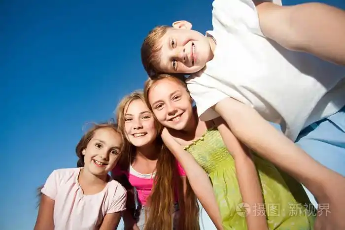 四个快乐美丽的孩子们看着相机从顶在阳光灿烂的夏天的一天蓝蓝的天空