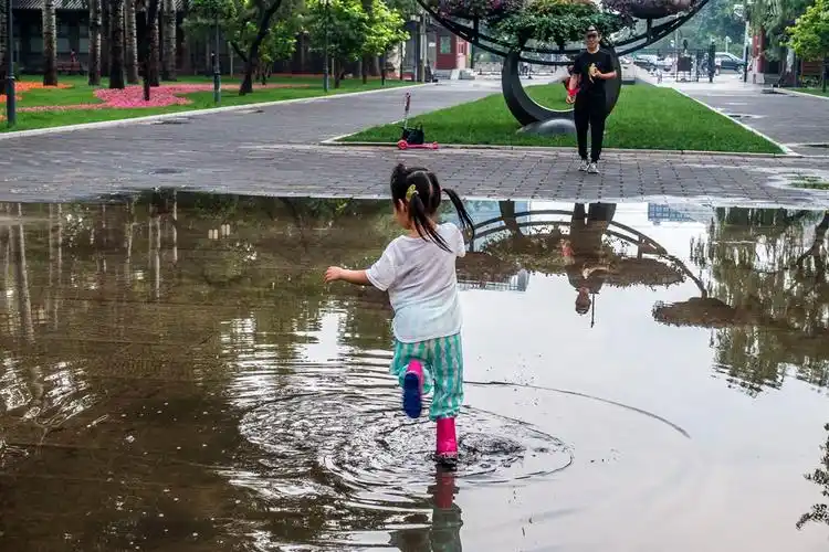 一个小女孩穿着红雨靴在水坑中跳舞.