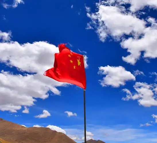 公园门口的五星红旗在蓝天白云下迎风招展,鲜艳夺目,彰显了祖国的雄姿