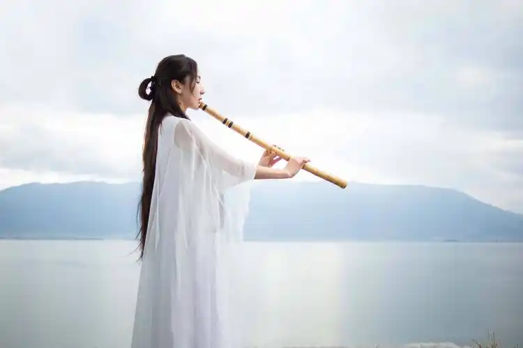 古风时尚大片,照片中娄艺潇一袭垂坠感十足的白色长裙,手执长箫在水边