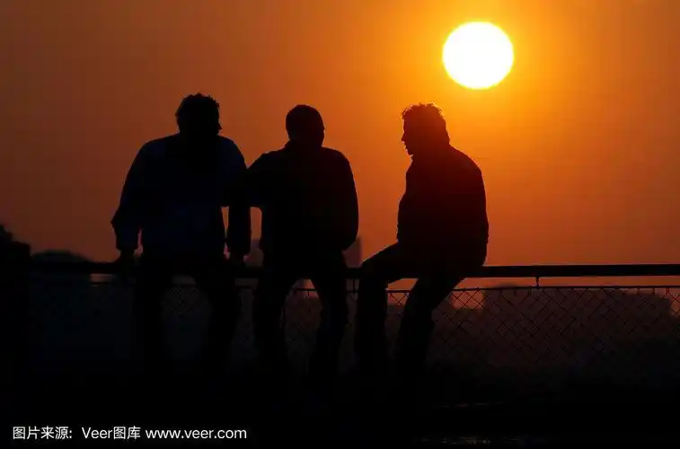日落时分,三个男性朋友的剪影坐在篱笆上