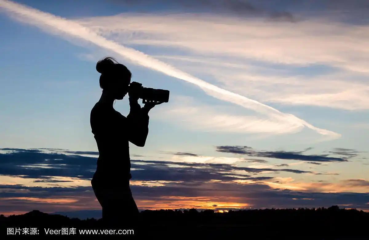 一个女孩正在用单反相机拍摄日落天空的剪影.
