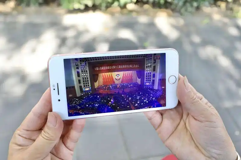 一名值勤的志愿者通过手机观看全国政协十三届三次会议闭幕会直播