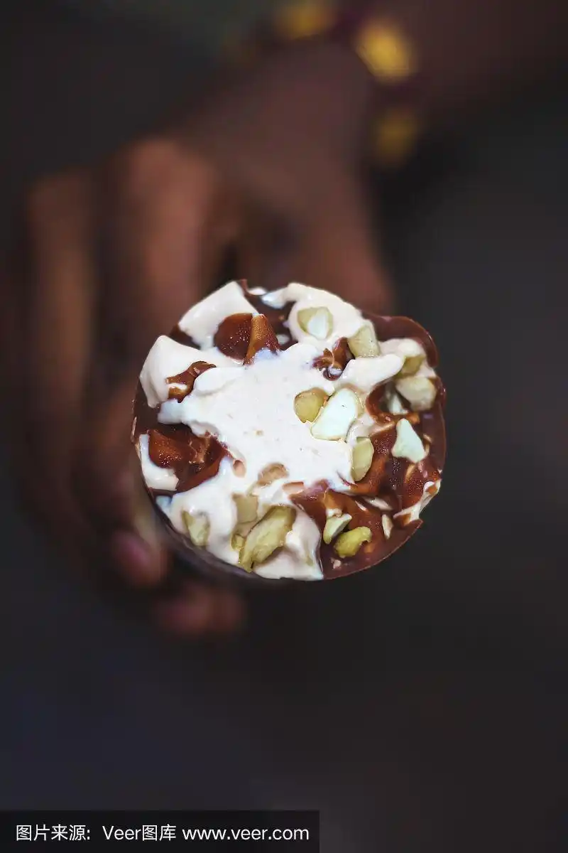 一个男孩手里拿着一个奶油糖果冰淇淋蛋筒,背景是黑色的腰果冰淇淋.