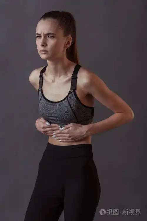 穿着运动服的漂亮女孩摸着她的肚子感到疼痛灰色背景