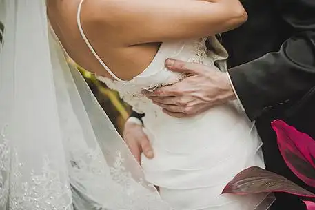 男人抱住身着白色连衣裙的女人,腰和屁股. 新娘的背影.