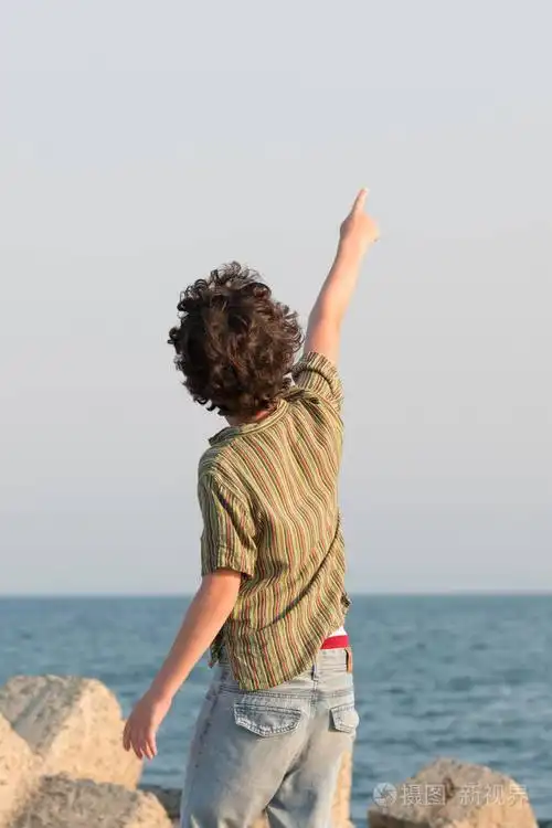 这个男孩站在面对大海的码头上,把手指向天空.