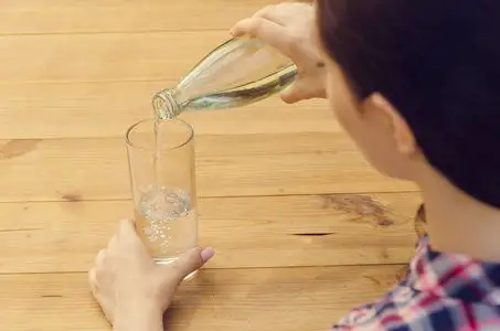 年轻漂亮的女人,在休闲衬衫倒水入杯照片