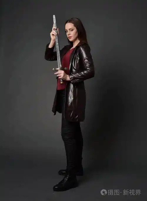 穿红色长皮杰克的黑发女孩的全长肖像站立姿势手持剑在灰色工作室背景