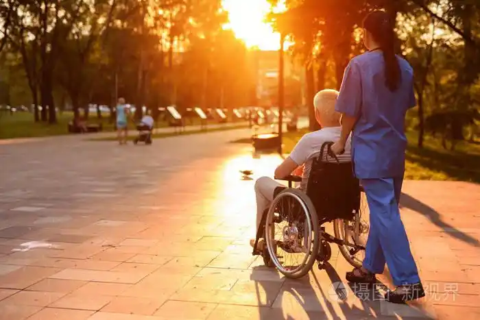 一个护士和一个老人坐在轮椅漫步在公园在日落