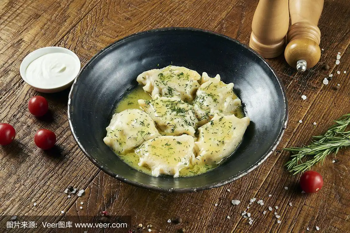 用黄油煮过的乌克兰饺子,肉配上绿色蔬菜和酸奶油,放在一个黑色的碗里