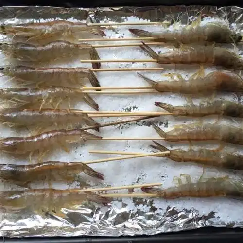 第3步,烤盘中铺上锡纸,洒满大粒海盐,将串好的虾排放在盐上